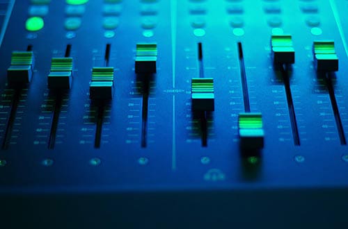 Sliders in various positions on a control panel with green and blue lighting